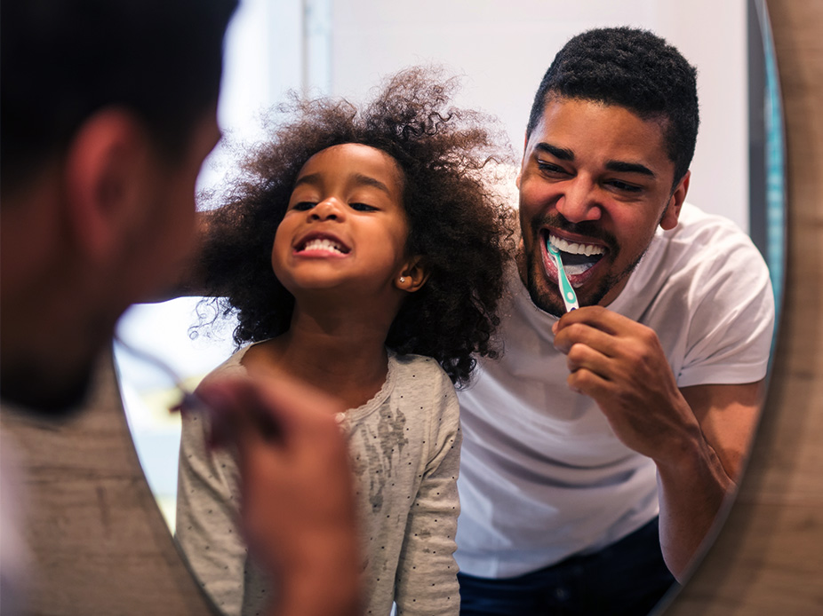 Father and daughter brushing their teeth in front of the bathroom mirror.